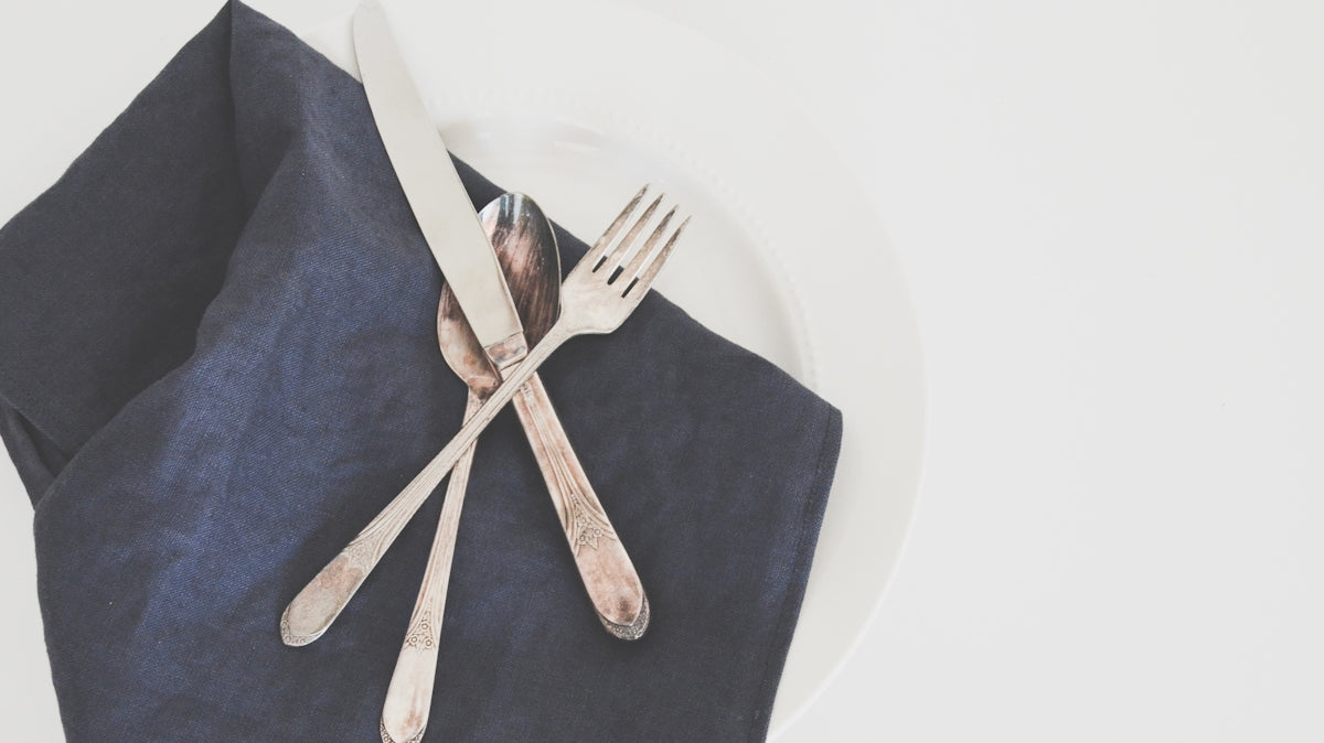 gray fork, spoon, and butter knife on plate with black table napkin