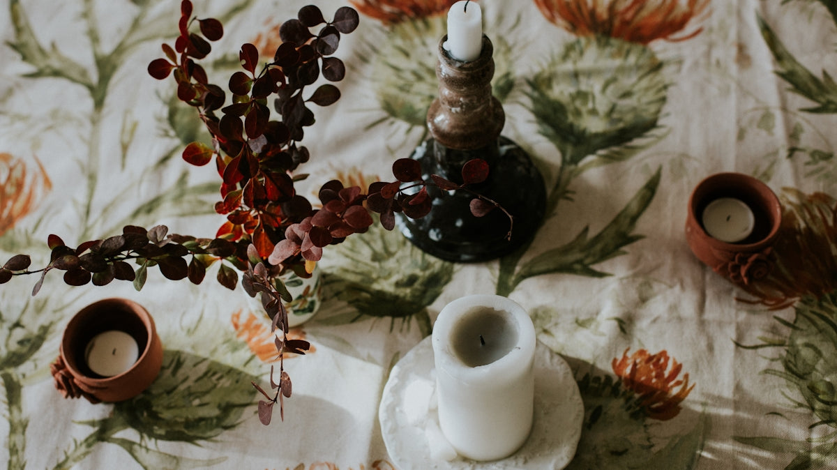 Decorative candle holder with white candle on floral tablecloth featuring red and green patterns.