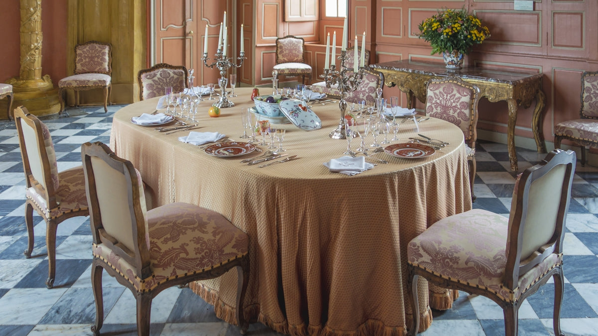 Elegant dining table setting with a beige tablecloth and ornate chairs.