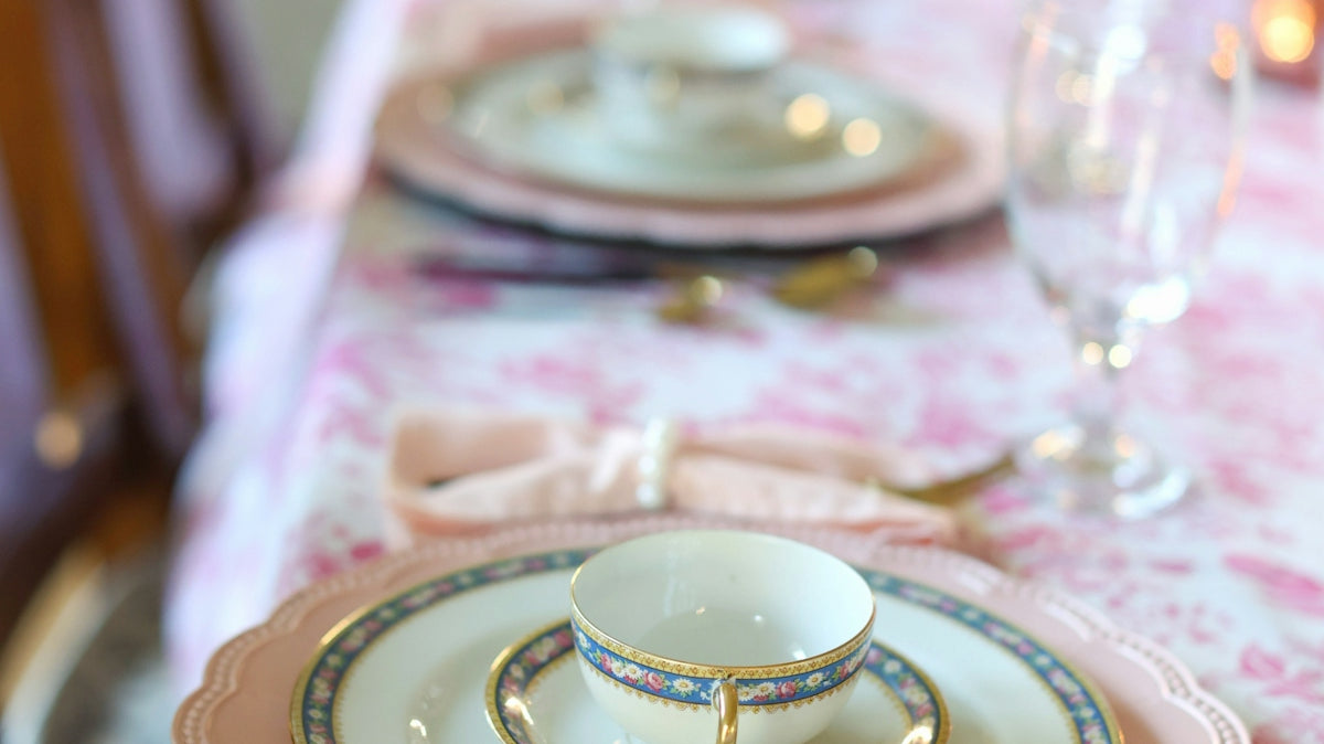Elegant place setting on a floral, pink tablecloth.