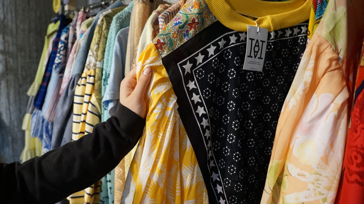 A hand selecting clothes from a rack in a store.