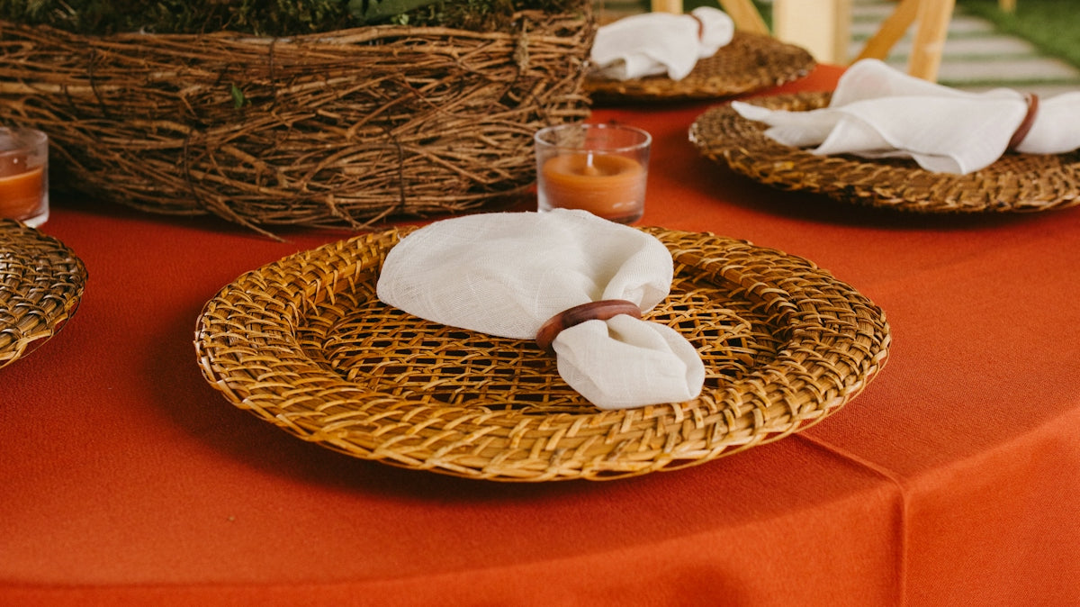 Orange tablecloth with woven placemats, white napkins, and orange flowers.