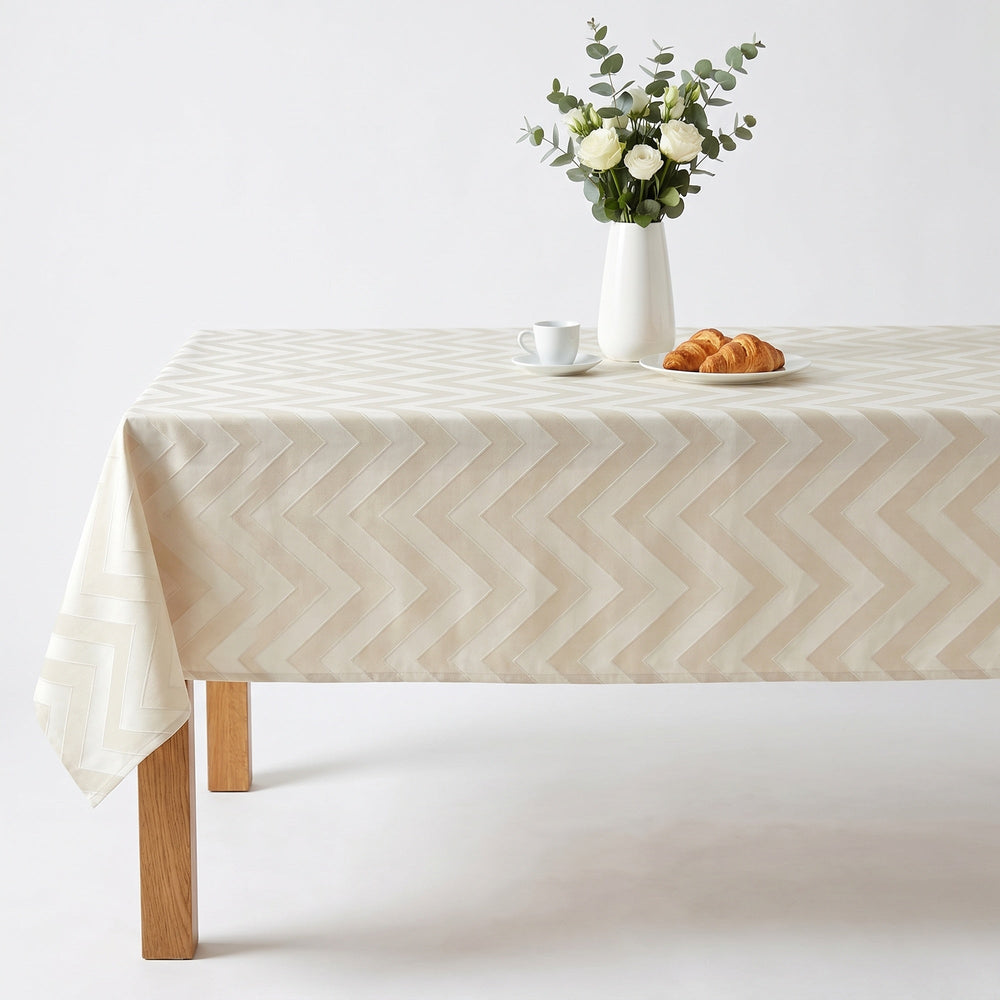 Chevron Tablecloth in cream color with a zigzag pattern, elegantly draped over a wooden table.