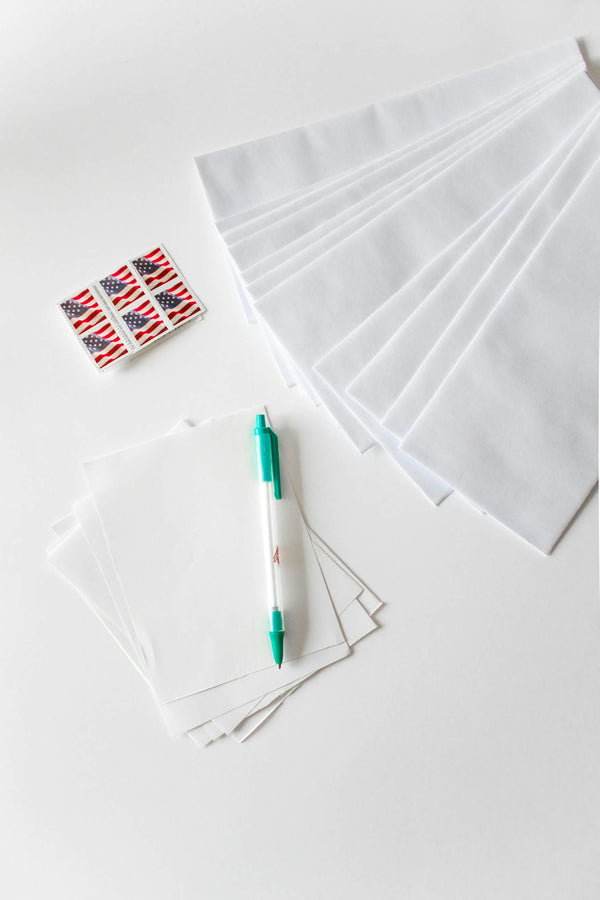 White stationery set with envelopes, blank sheets, and a green pen for writing.