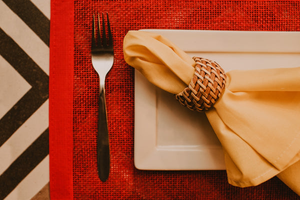 Elegant table setting with a white plate, yellow napkin, and woven napkin ring.