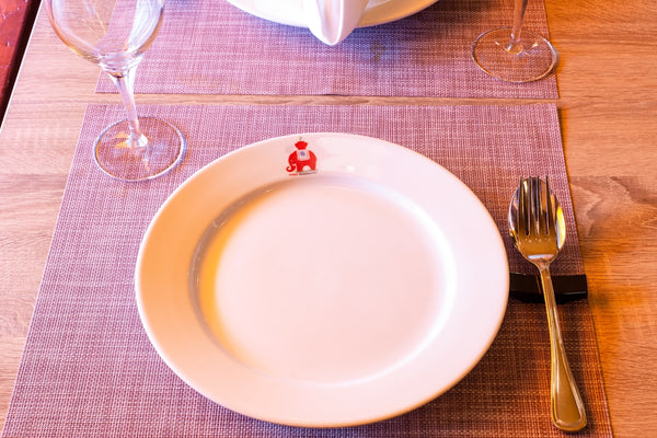Elegant white dinner plate with a red logo, set on a stylish table with glassware.