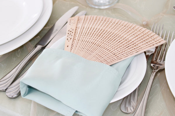 Elegant fan placed on a soft mint napkin at a dining table setting.