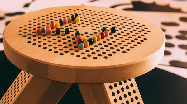 Colorful wooden stool with perforated top and decorative beads arranged on it.