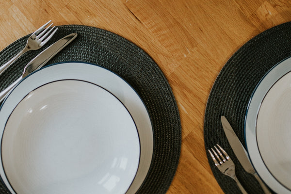 Elegant white dinner plates with a black rim on woven placemats.
