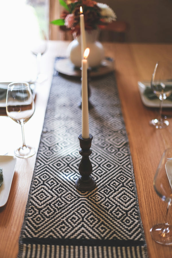 Black and white geometric table runner enhancing a dining table setting with candles and glassware.