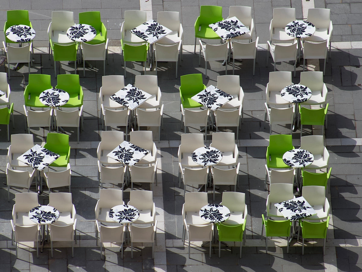 Outdoor dining tables with green and white chairs arranged in a modern setting.