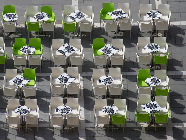 Outdoor dining tables with green and white chairs arranged in a modern setting.