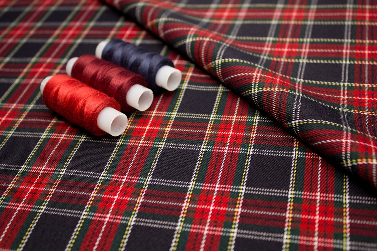 Tartan fabric featuring red, green, and black plaid pattern with spools of red and navy thread.