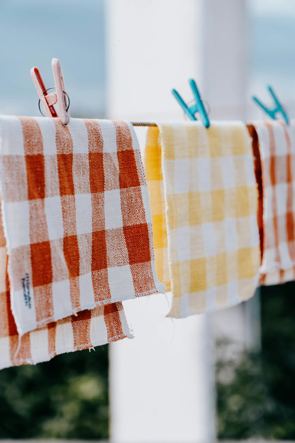 Checkered kitchen towels in orange and yellow hanging on a clothesline.
