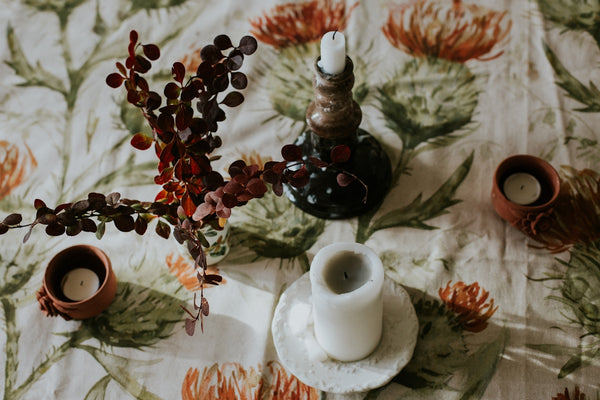 Decorative candle holder with white candle on floral tablecloth featuring red and green patterns.