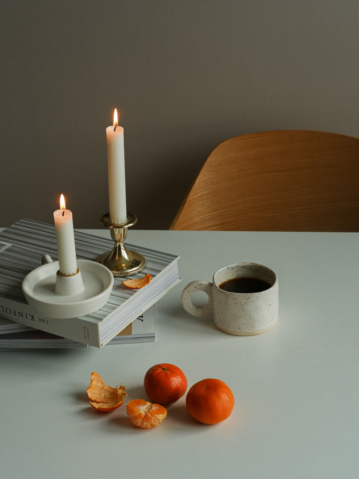 Candle holders with candles and a coffee cup on a table featuring tangerines and books.