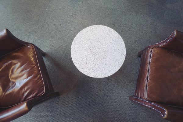 Terrazzo coffee table surrounded by two brown leather chairs in a cozy setting.