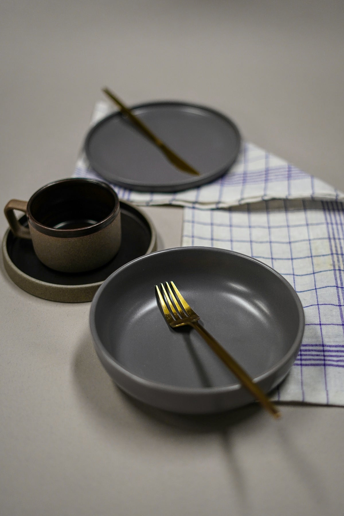 Elegant gray dinnerware set featuring a bowl and plate with gold fork and cup.