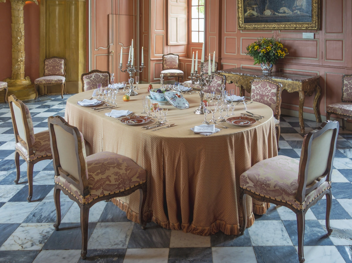 Elegant dining table setting with a beige tablecloth and ornate chairs.