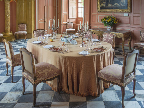 Elegant dining table setting with a beige tablecloth and ornate chairs.