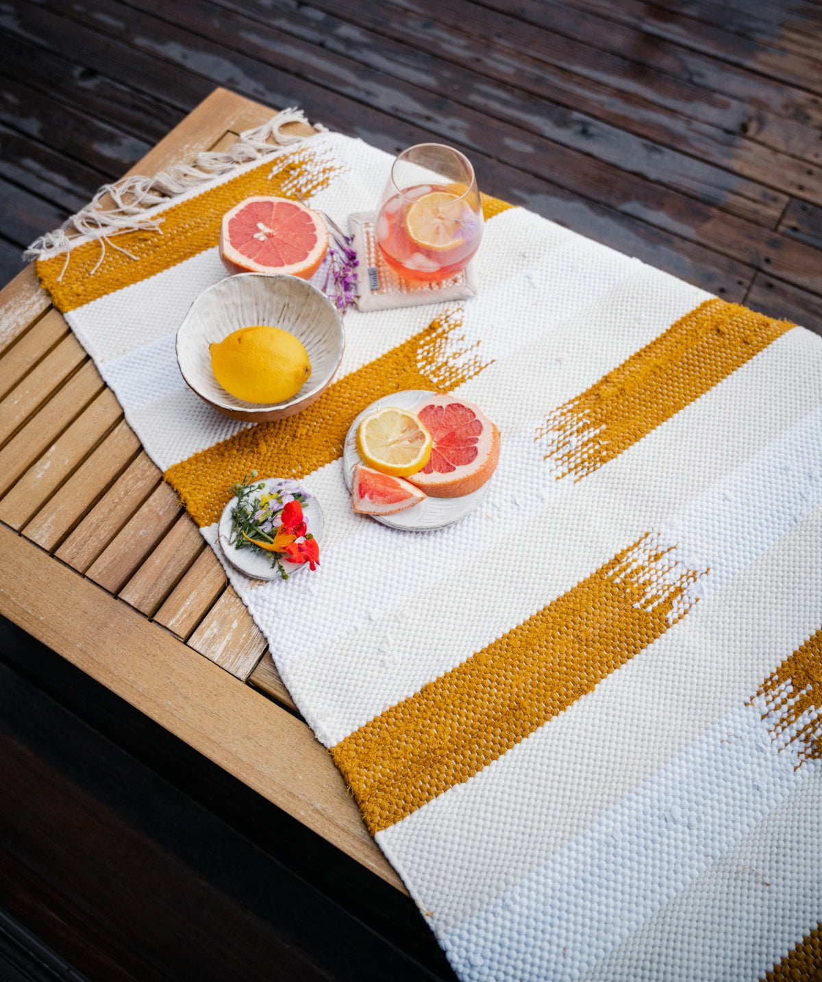Striped table runner with yellow and white patterns, featuring fruits and drinks on a wooden table.