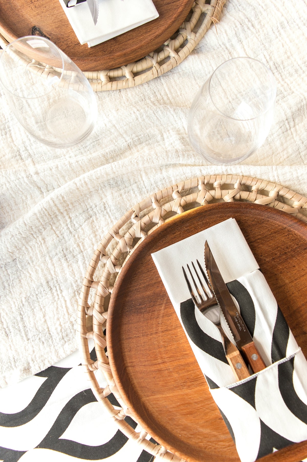 Elegant table setting with black and white napkin, wooden plates, and glassware.