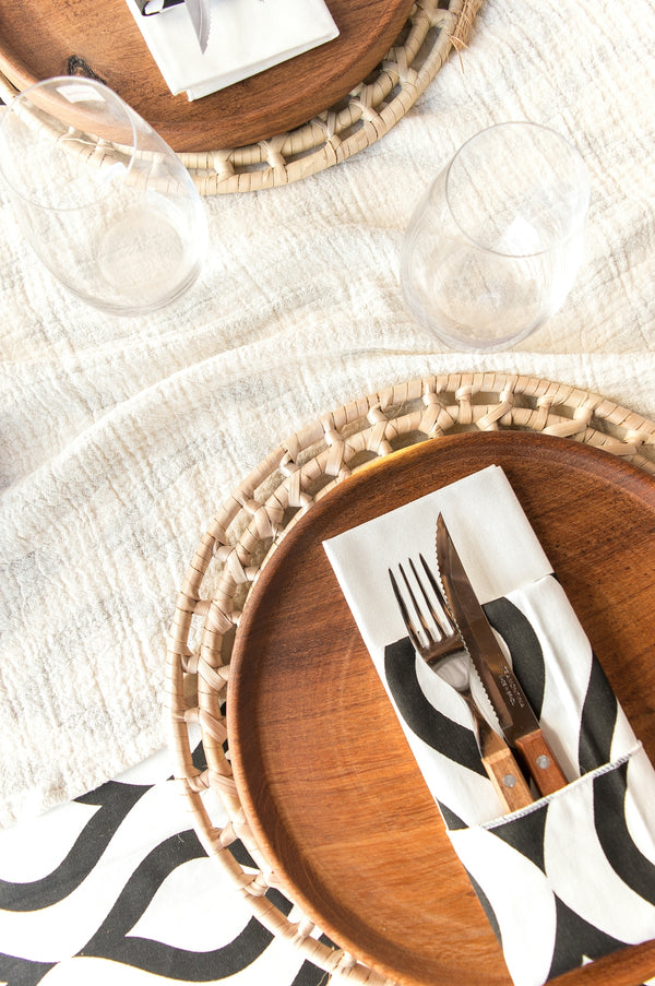 Elegant table setting with black and white napkin, wooden plates, and glassware.