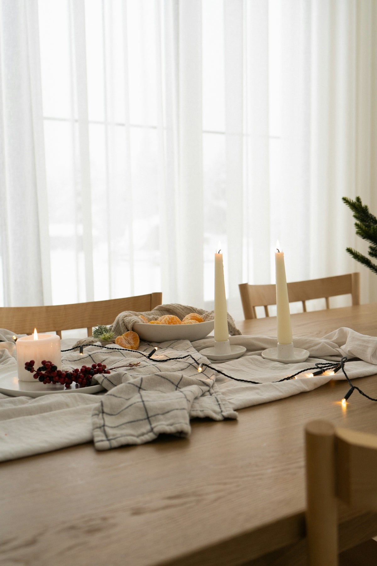 Elegant dining table setting with white candles, a bowl of fruit, and festive decorations.