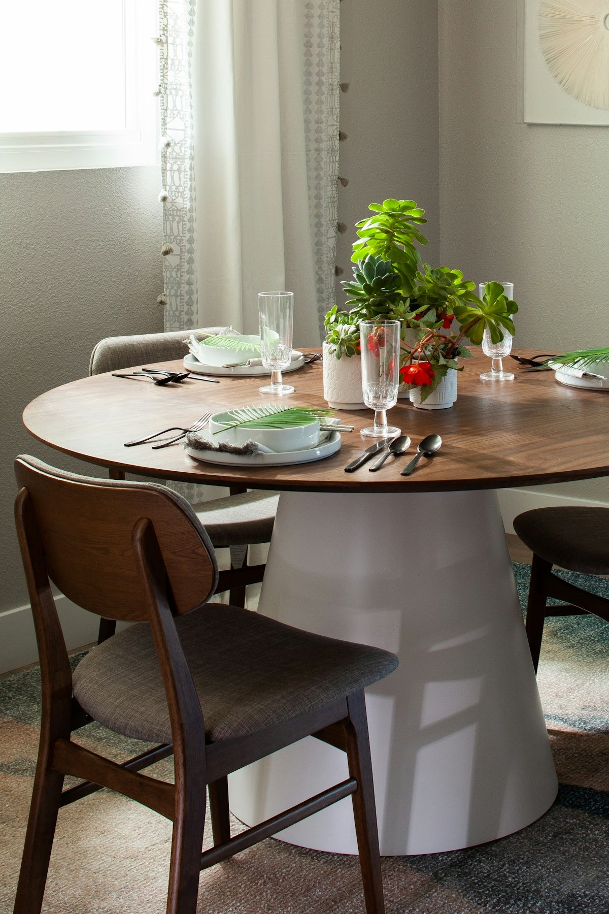 Modern round dining table with a white base, set for a meal with green plates and plants.