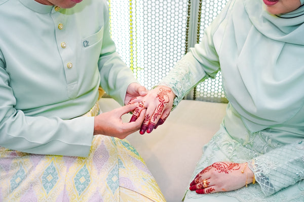 Traditional wedding ceremony featuring a couple in matching pastel outfits with intricate henna designs.