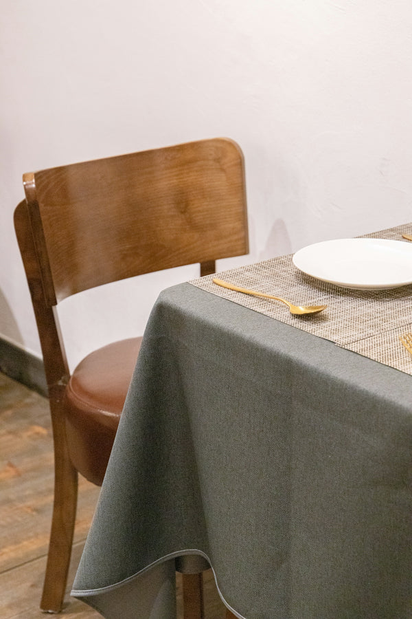 Wooden dining chair beside a gray tablecloth with a plate and cutlery.