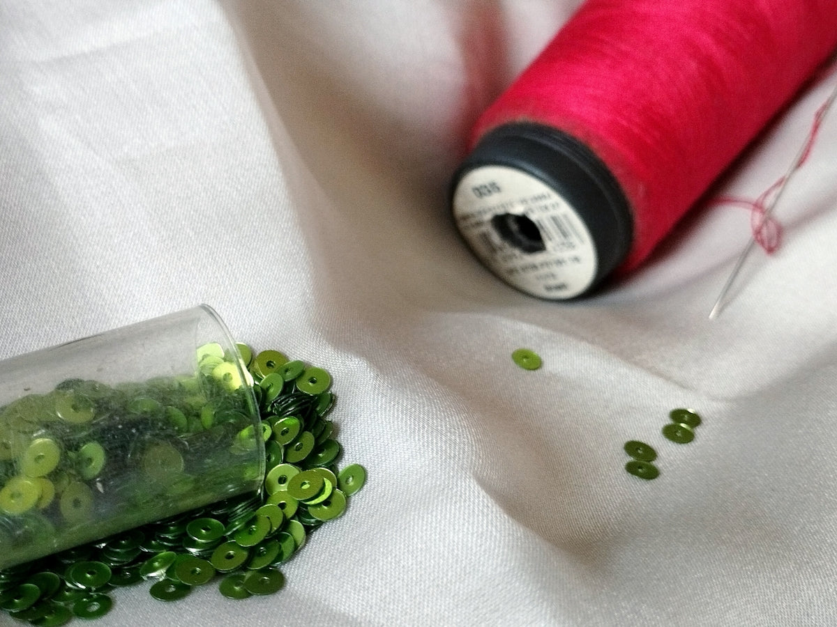 Green Sequin Crafting Supplies with Pink Thread for DIY Projects.