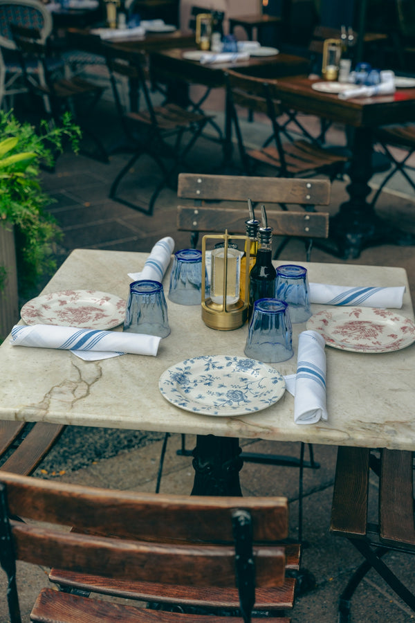 Dining table setup with floral plates and blue glasses for an outdoor restaurant experience.