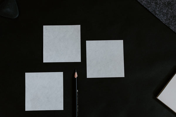 Blank Sticky Notes set on a dark surface with a pencil beside them.