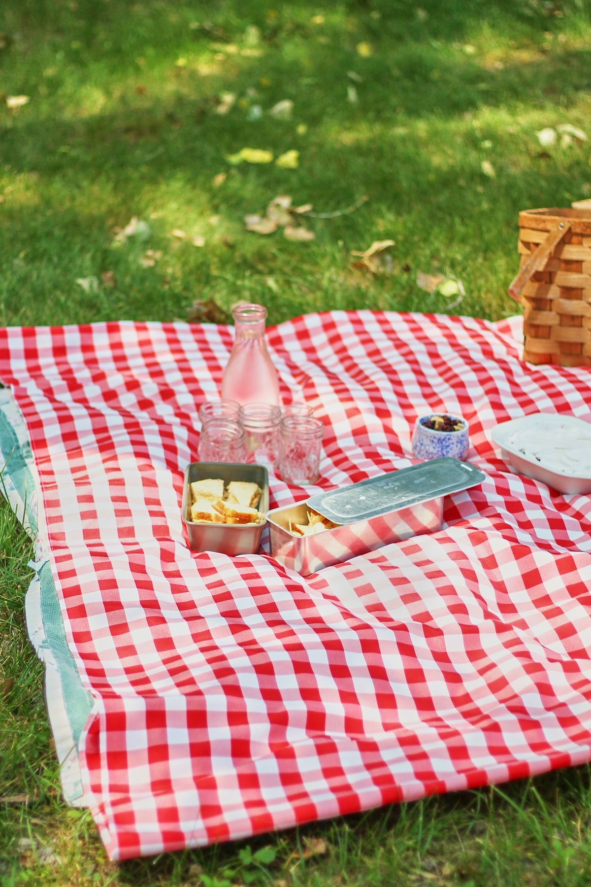 Picnic blanket with red and white checkered pattern, featuring snacks and drinks.