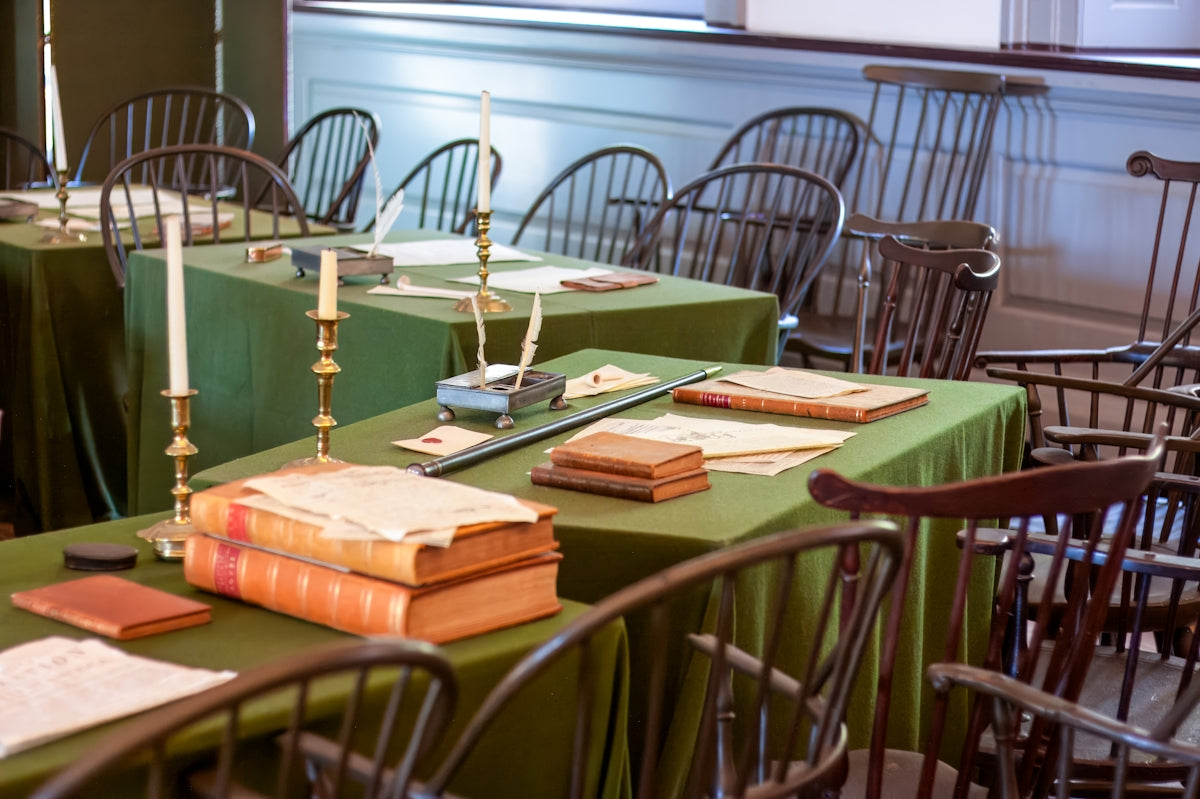 Historic meeting room setup with green tables, books, and candles.