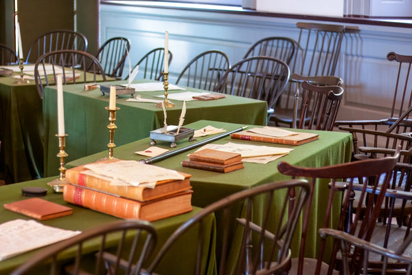 Historic meeting room setup with green tables, books, and candles.