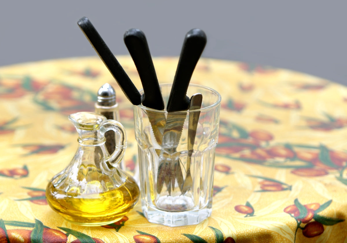 Olive oil dispenser with black utensils in a glass on a colorful tablecloth.