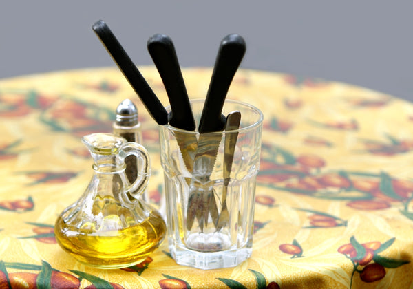 Olive oil dispenser with black utensils in a glass on a colorful tablecloth.