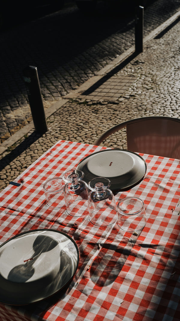 Table setting with white plates and glassware on a red and white checkered tablecloth.