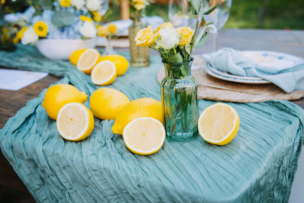 Lemon centerpiece with fresh lemons and flowers on a teal tablecloth.
