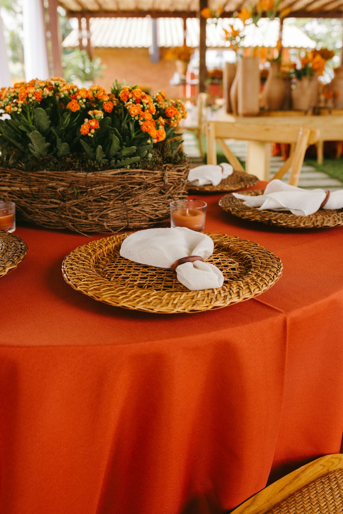Orange tablecloth with woven placemats, white napkins, and orange flowers.