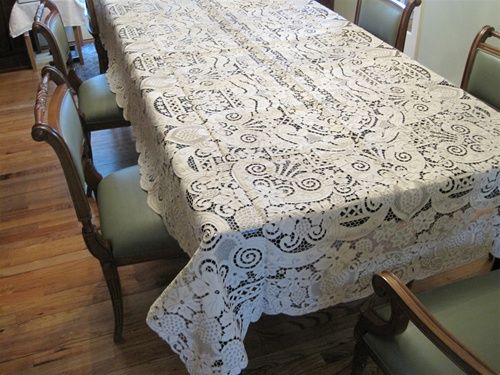 Ivory hand-embroidered linen lace tablecloth with dense floral cutwork on a dining table