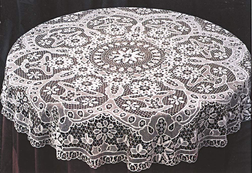 White openwork lace tablecloth with a central rosette medallion and deep scalloped border on a dark surface