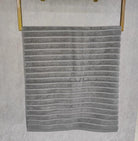 Silver-gray terry towel with a raised ribbed stripe texture hanging on a gold rail
