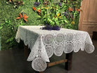 White medallion lace tablecloth with round rosette motifs and a scalloped edge on a wood table
