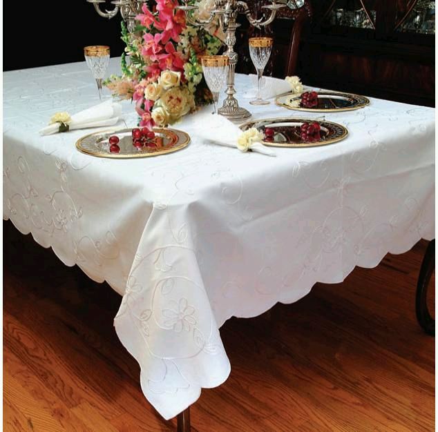 White tablecloth embroidered edge-to-edge with white scrolling vinework and small flowers, scalloped edge