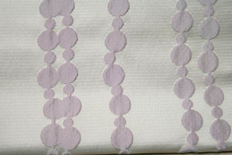 White fabric with lavender circular patterns, ideal for home decor projects.